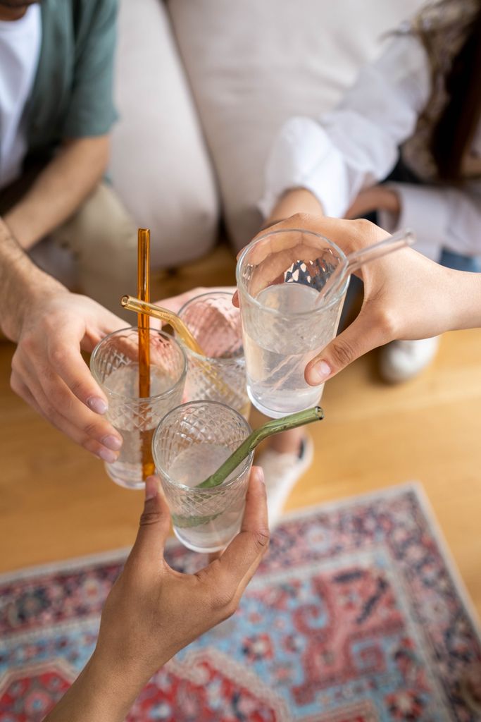 Above view of friends toasting with glasses of water and amazon find of reusable glass straws with brush