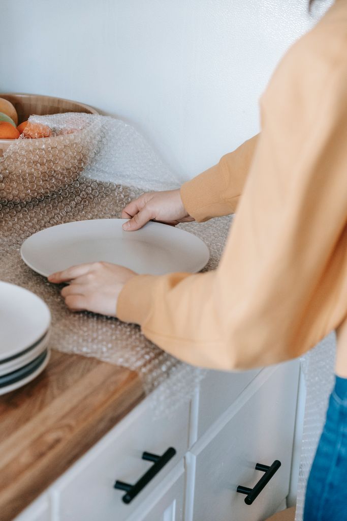 Close-up of a woman packing plates with bubble wrap on a kitchen counter, preparing for moving home