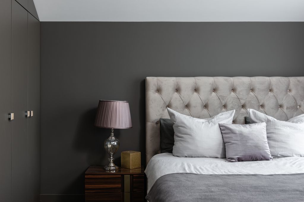 Comfortable bed with soft cushions placed near lamp on bedside table in stylish bedroom with closer and gray wall at home