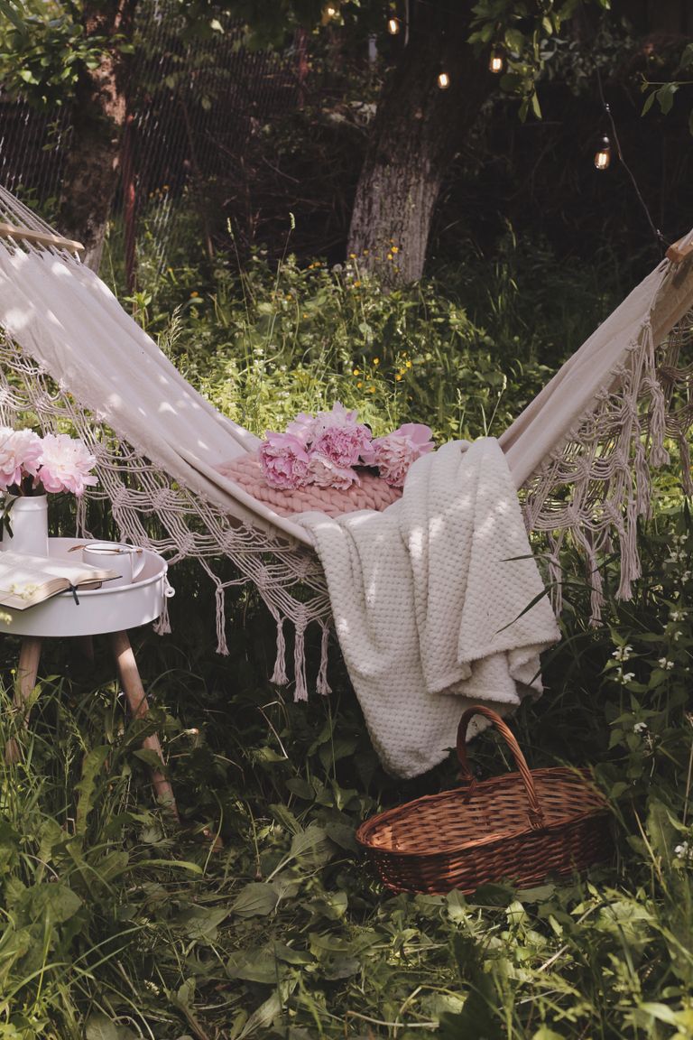 Cozy garden hammock with pink flowers, white blanket, and wicker basket for a backyard staycation garden