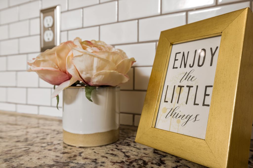 Gold-framed quote "Enjoy the little things" next to roses in a kitchen setting.