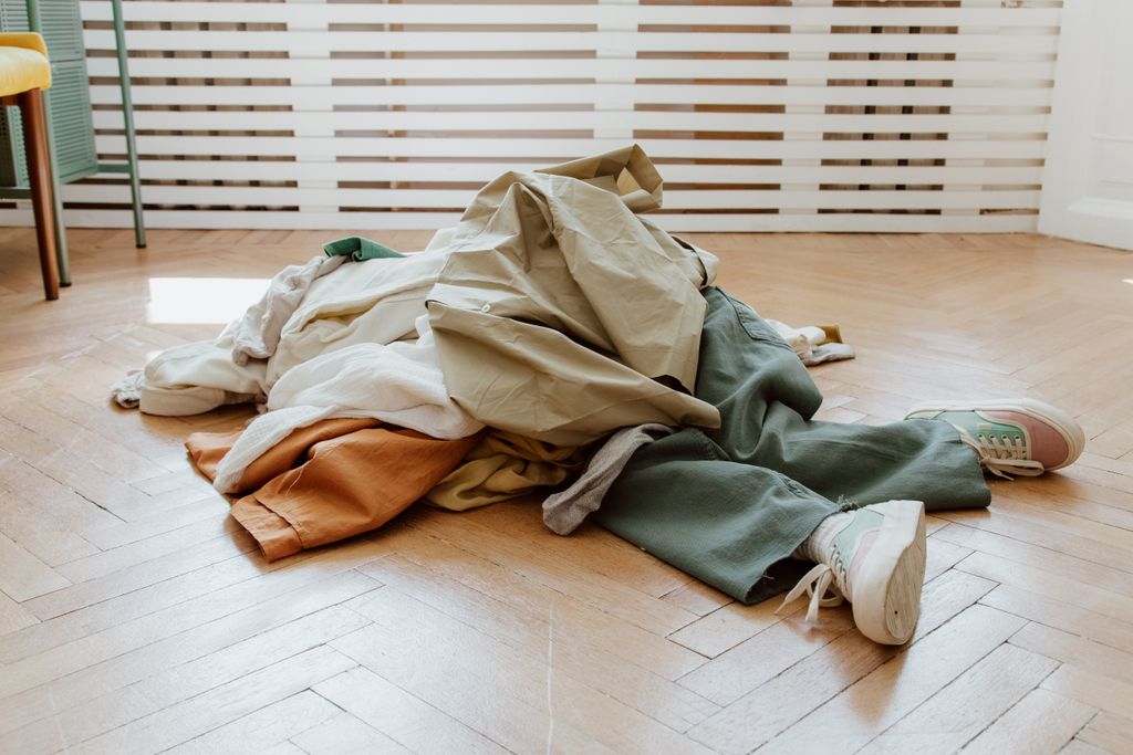 Pile of casual clothes on a wooden floor in a minimalistic entryway
