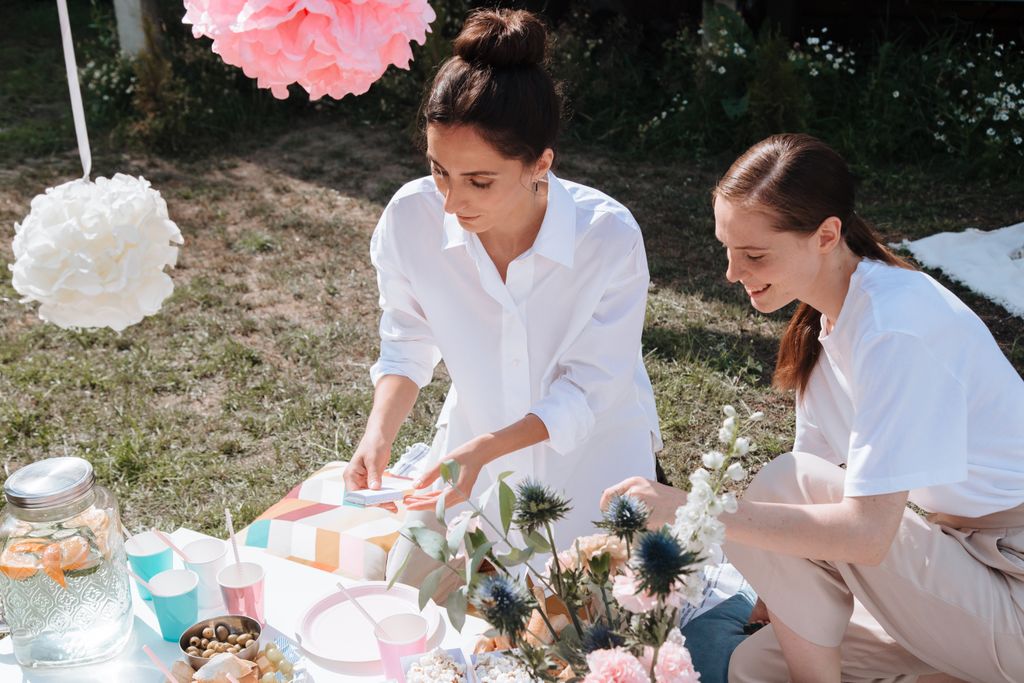 Two women setting up food and decorations for a summer garden party.