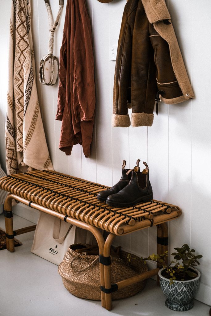 Warm and inviting entryway featuring a woven bench, hanging coats, and rustic decor on a white background.
