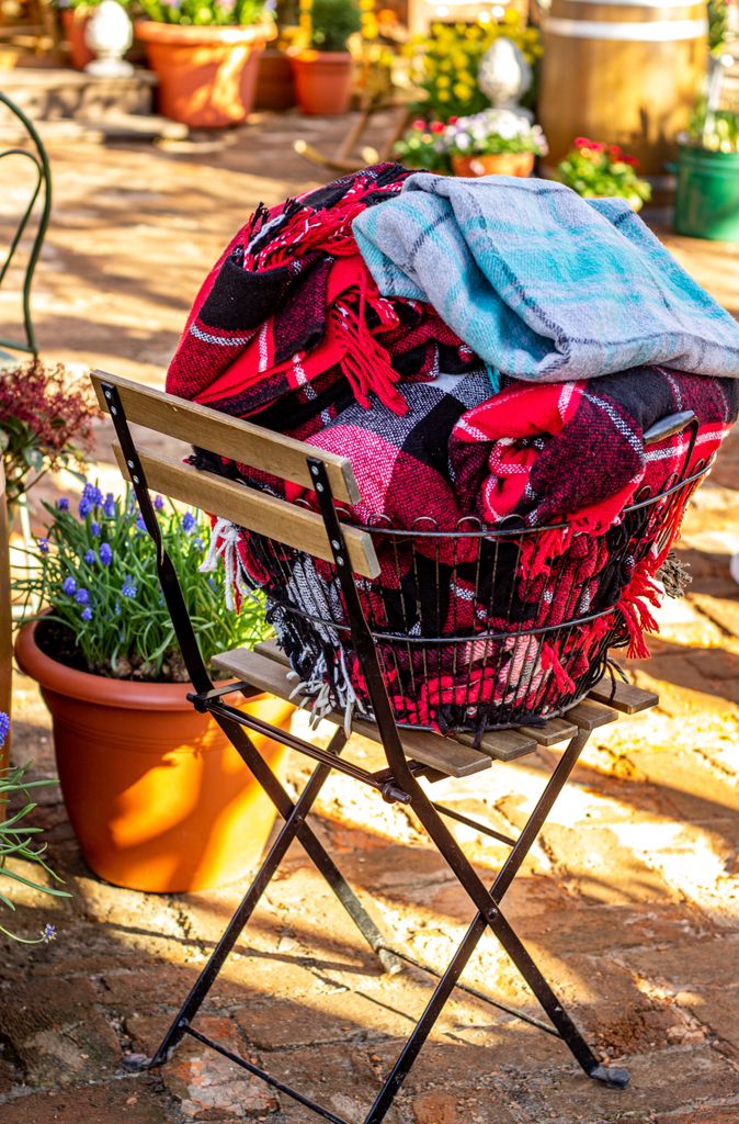 Folded colourful tartan blankets in basket outside in vibrant garden