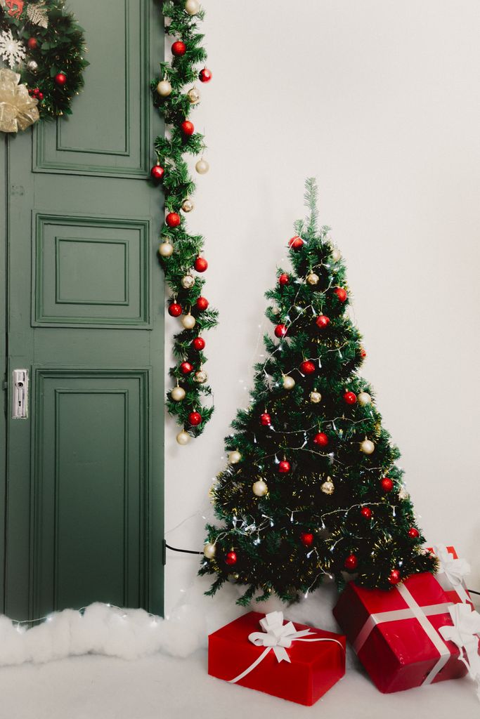 A beautifully decorated Christmas tree with red gifts beside a green door in Mexico City.