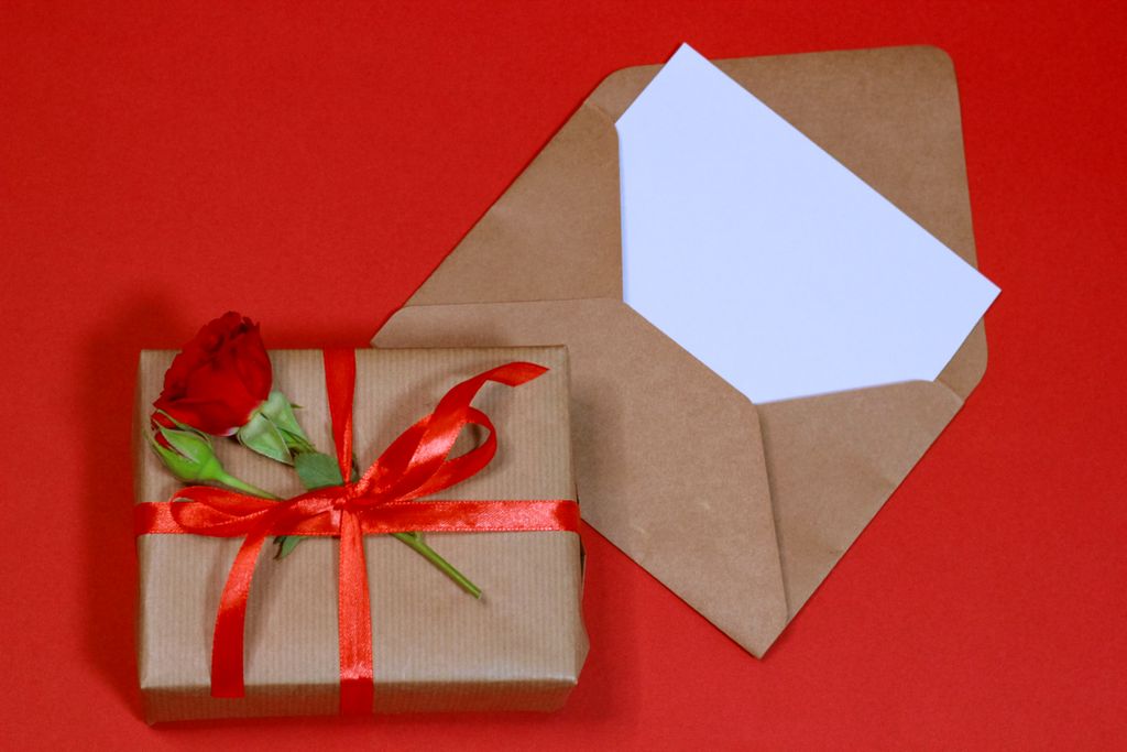 A beautifully wrapped gift box with a red rose on a vibrant red background, perfect for celebrations.