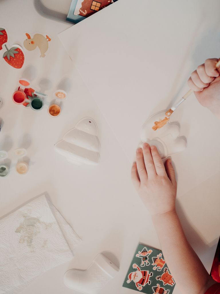 A child painting Christmas ceramic figurines at a table, experiencing creative holiday joy.