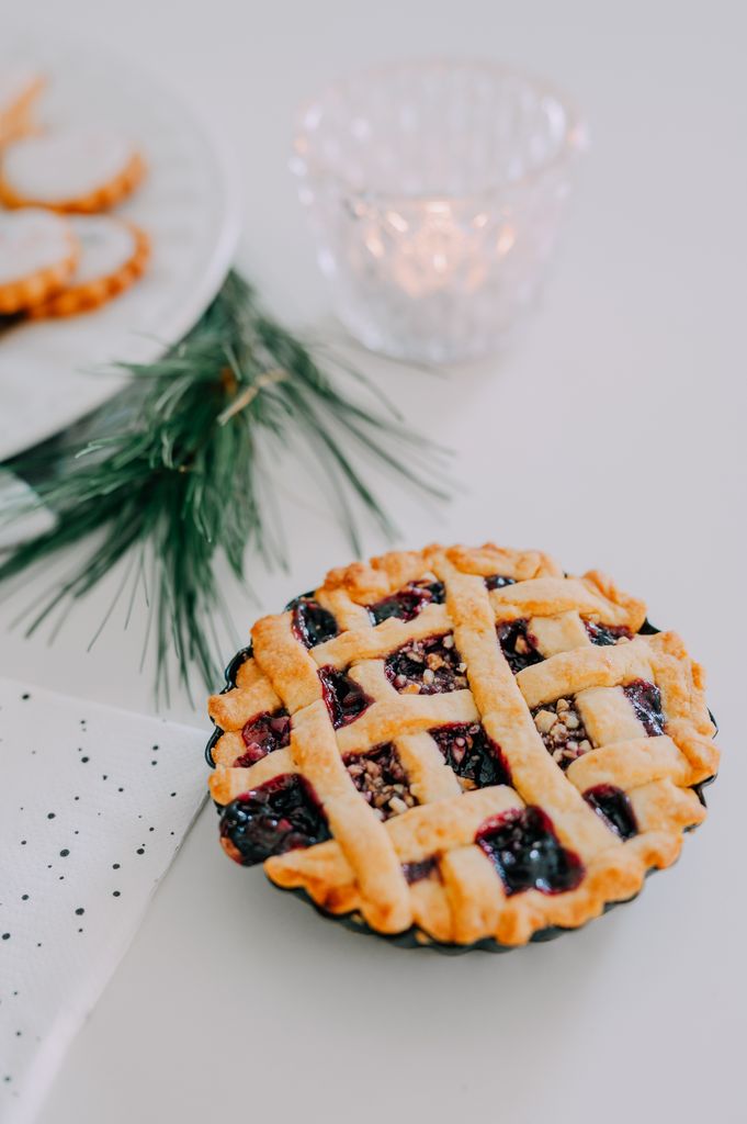 A close-up of a freshly baked berry pie with holiday decor and cookies.