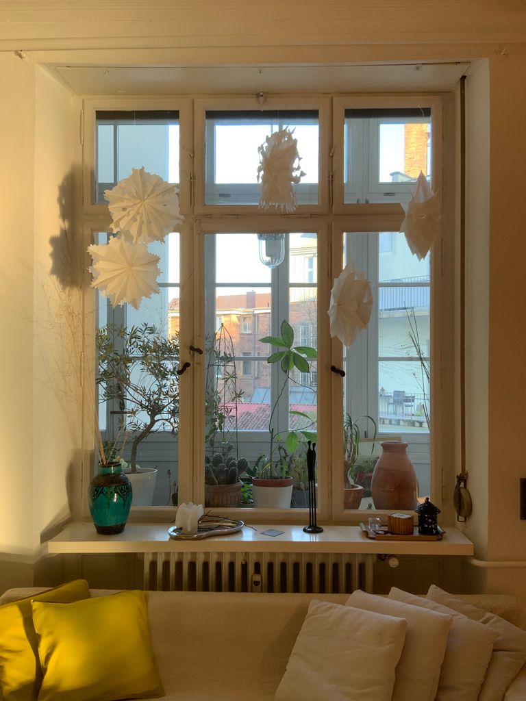 A cozy living room with a sunlit window, decorated with plants and paper ornaments.
