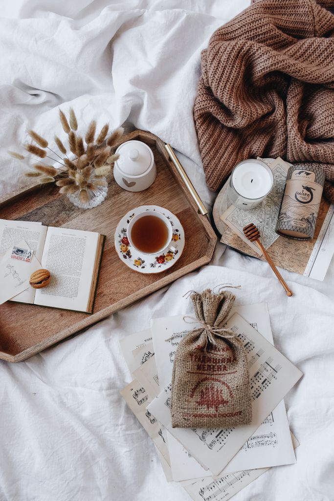 A cozy morning setup featuring tea, books, and a wooden tray on soft linen.