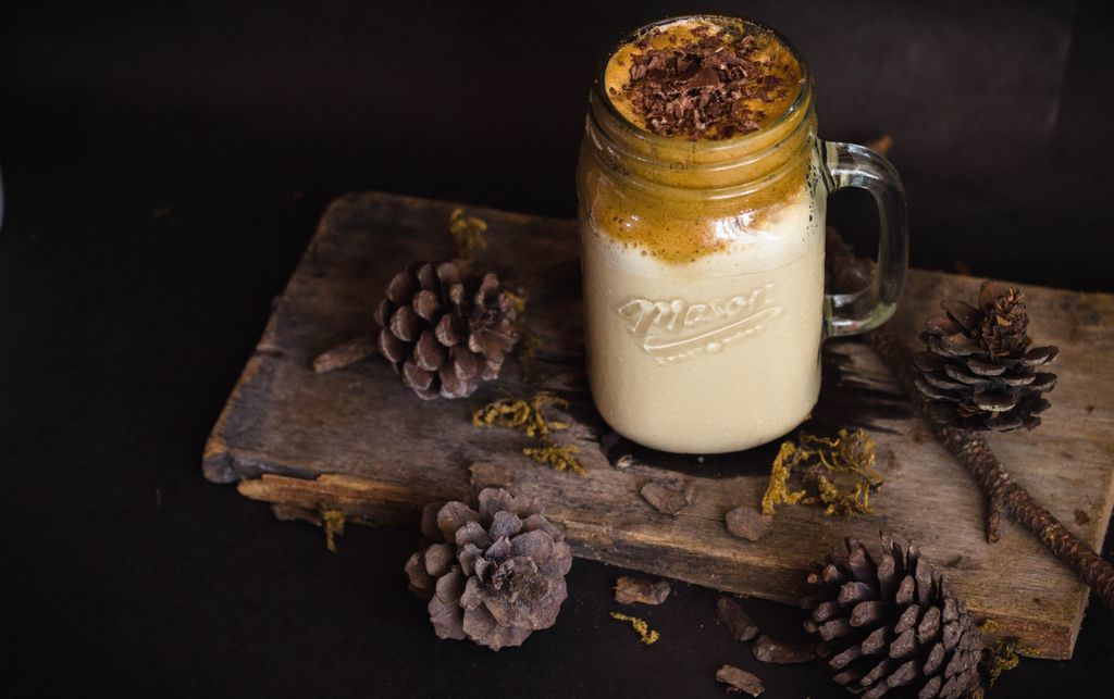 A creamy dalgona coffee on a wooden plank surrounded by pine cones for a warm, cozy vibe.