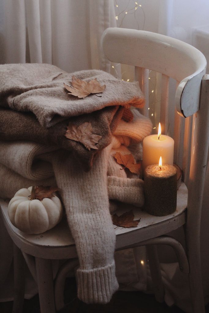 A warm autumn setup with cozy sweaters, candles, and a pumpkin on a chair.