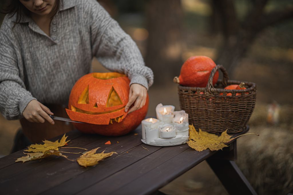 A woman carves a pumpkin into a Jack-o'-lantern amidst a cozy fall setting with candles.