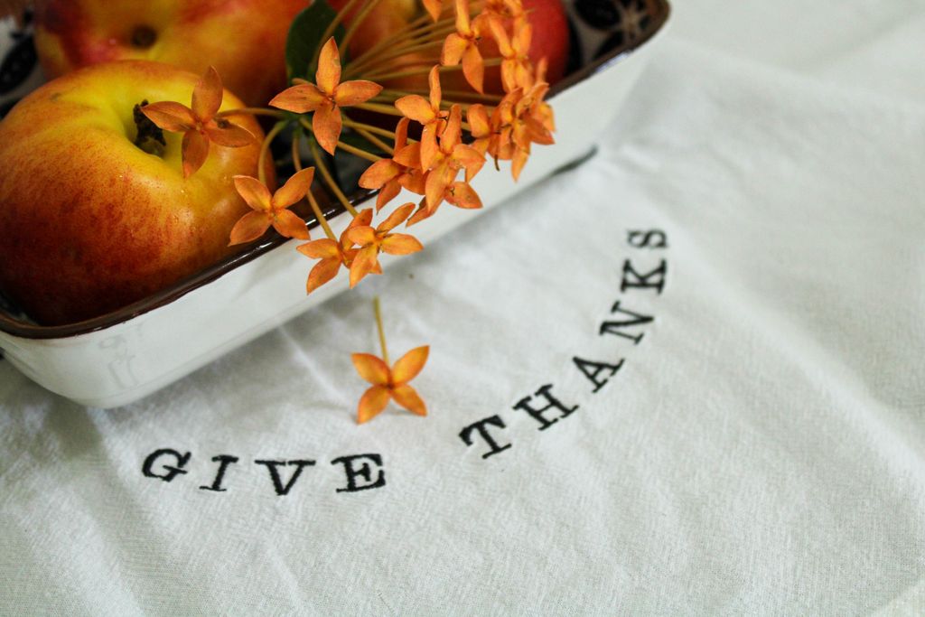 Artistic display of apples and orange flowers with 'Give Thanks' text on a white cloth, perfect for Thanksgiving decor.