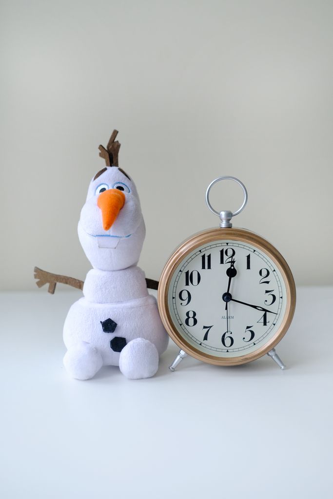 Charming Olaf toy sitting next to a vintage-style alarm clock, capturing playful nostalgia.
