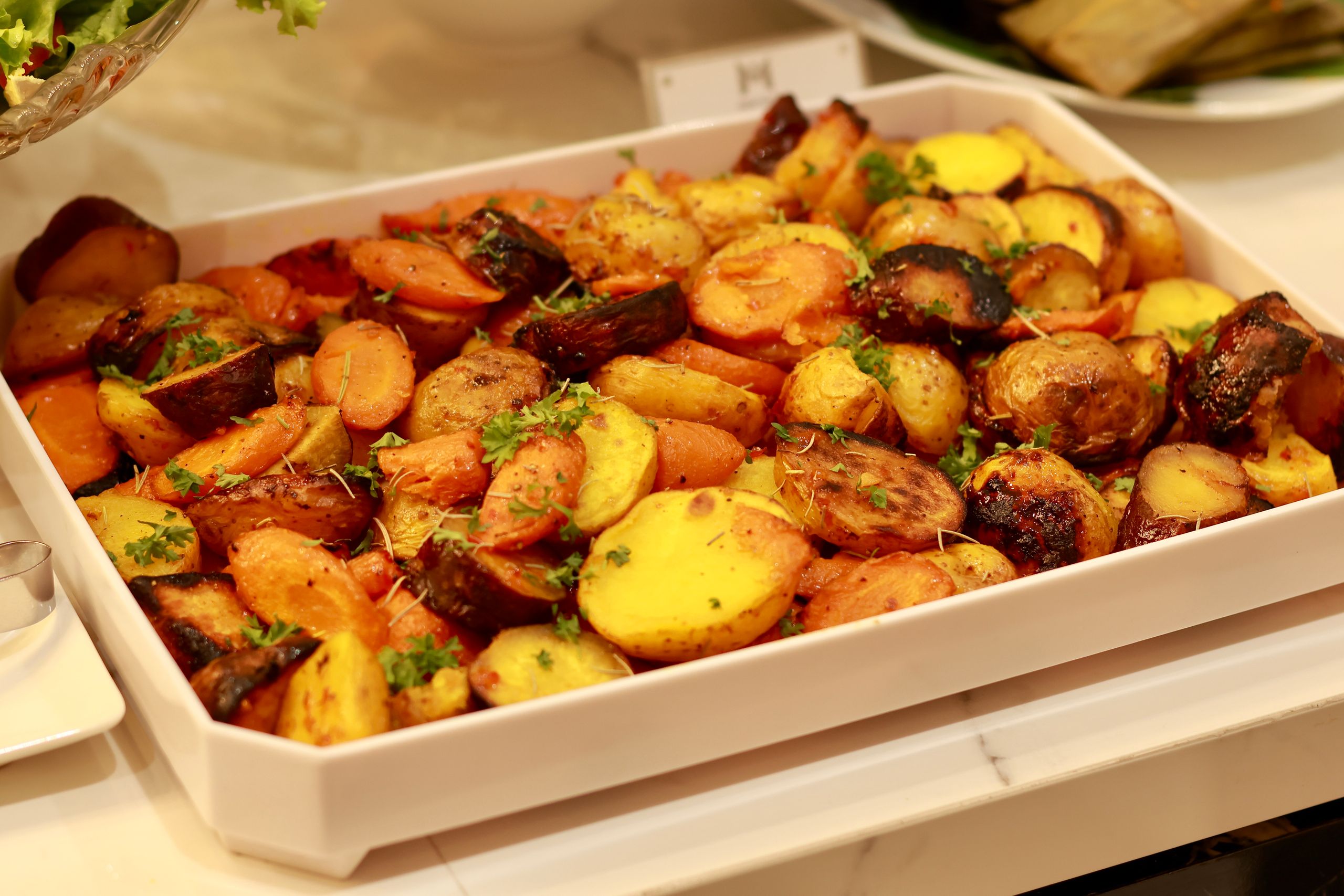 Colorful roasted potatoes and carrots garnished with herbs in a baking tray.
