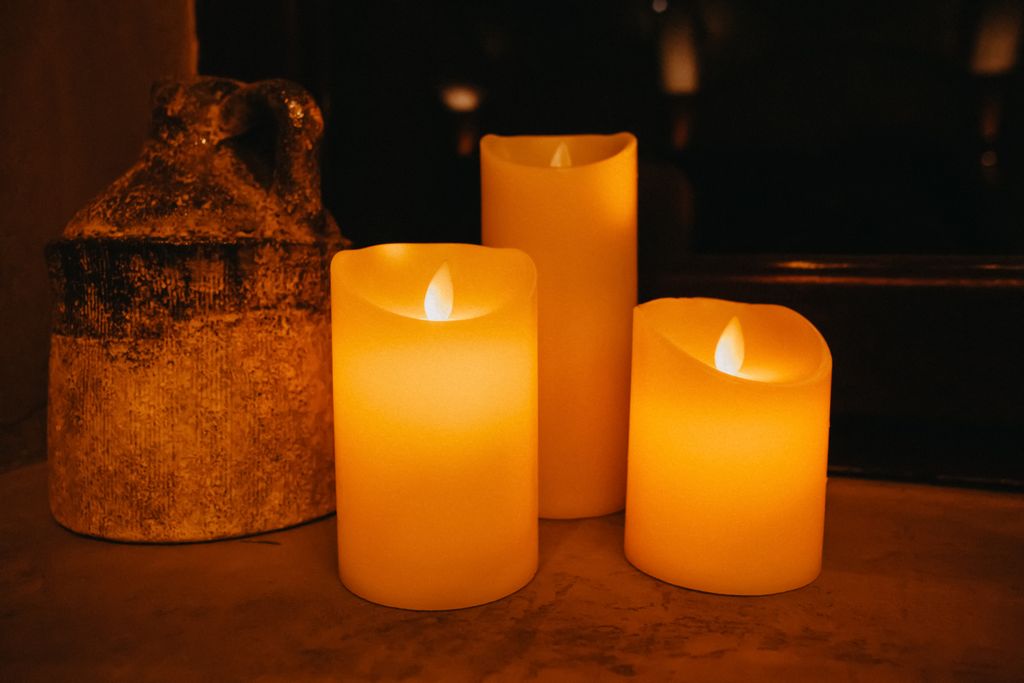 Decorative yellow burning candles placed near aged ceramic vase in dark room against blurred background