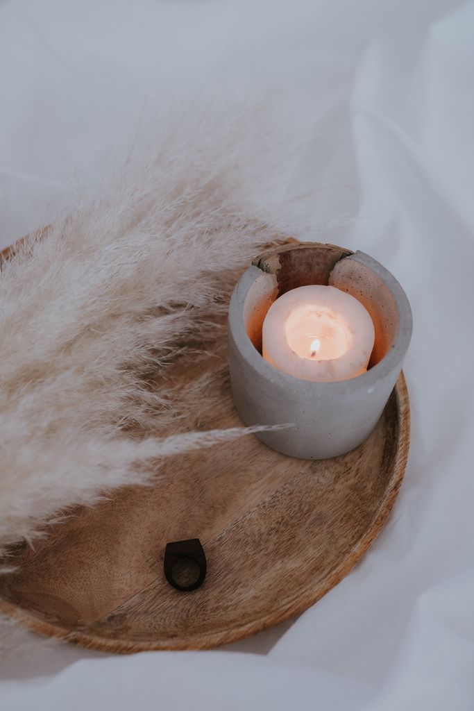 Elegant still life featuring a lit candle and dried pampas grass on a wooden tray.