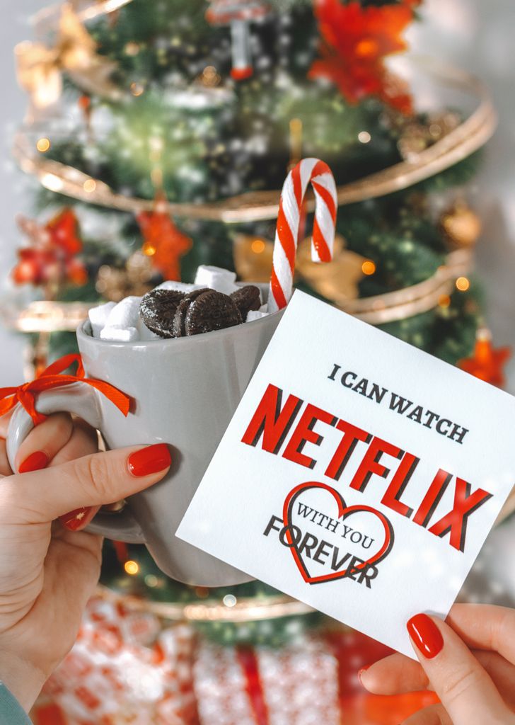 Festive Christmas card and hot chocolate with marshmallows in front of a decorated tree.