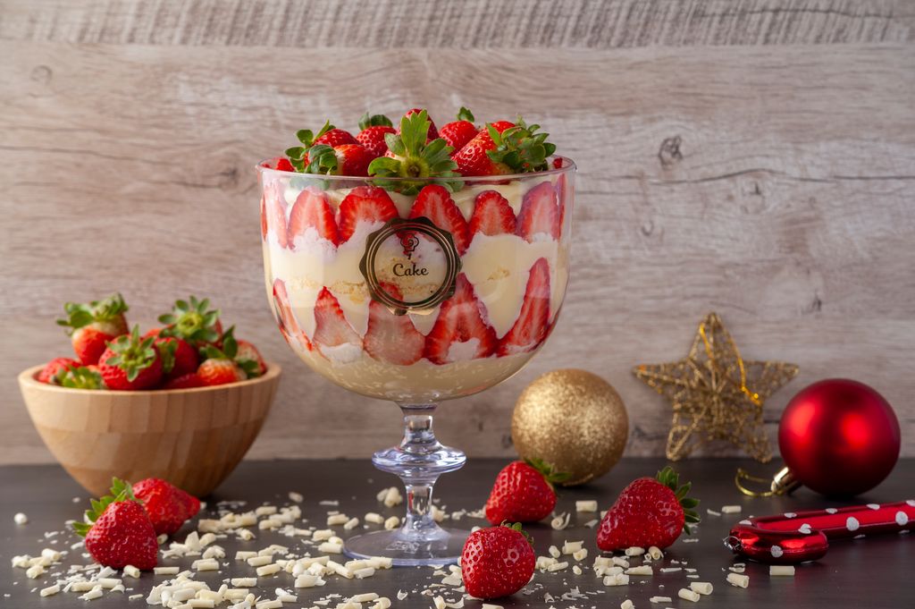 Festive strawberry trifle in a glass bowl surrounded by Christmas ornaments and fresh strawberries.