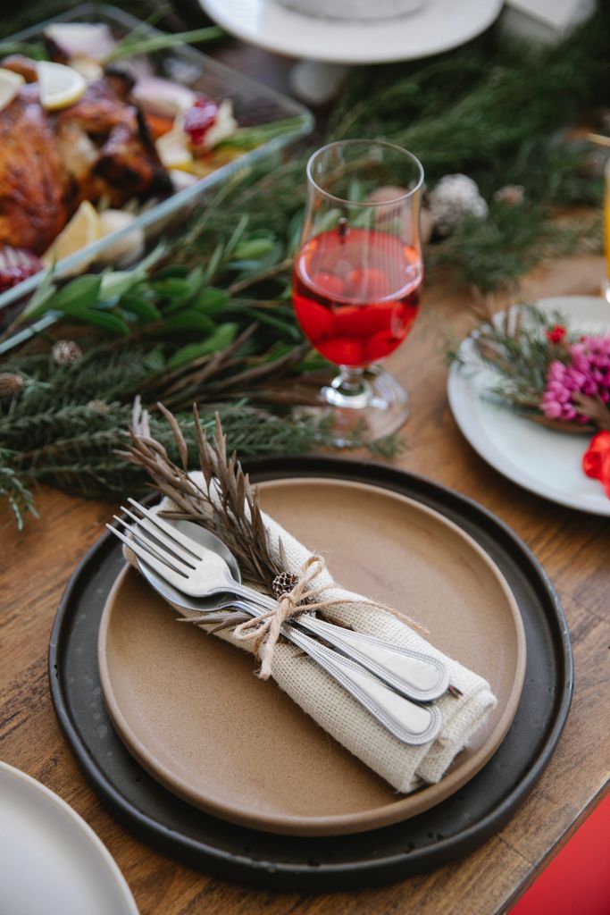 From above of served plates with cutlery and napkin tied ribbon with dry sprig near glass of wine and fir branch on festive table