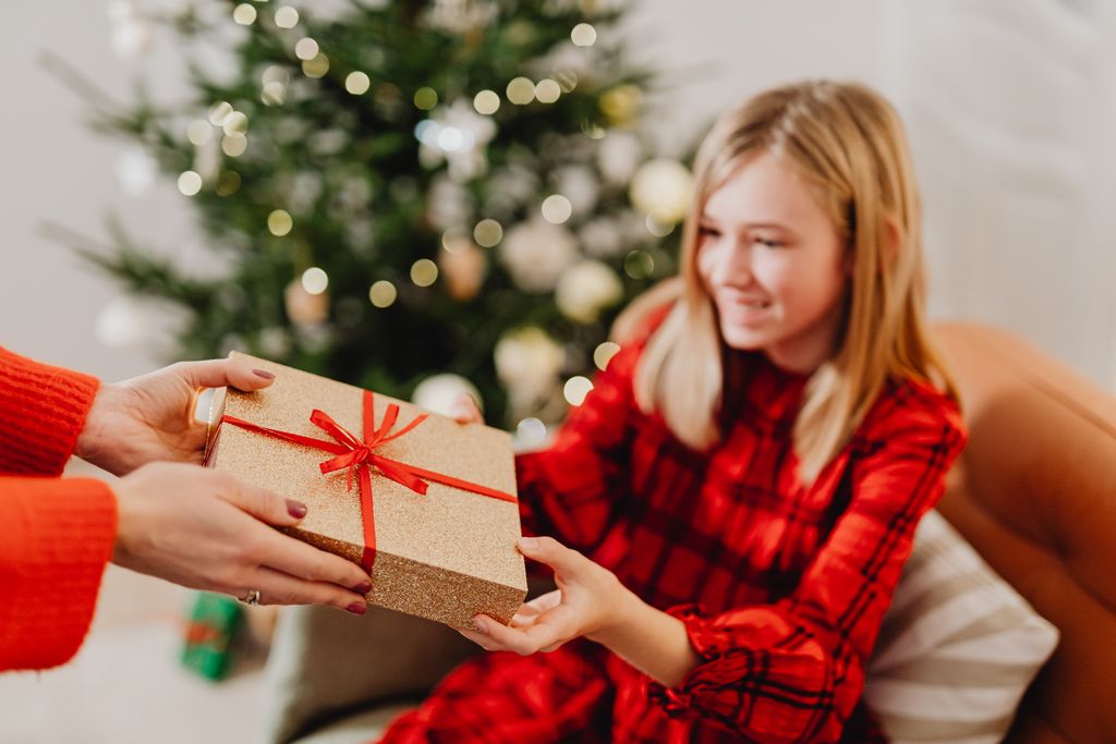 Christmas gifts for teenage girls handed over with happy face and christmas tree in the background