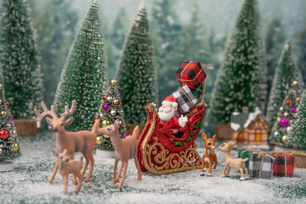 Miniature Christmas scene with Santa, reindeer, and gifts in a snowy forest.