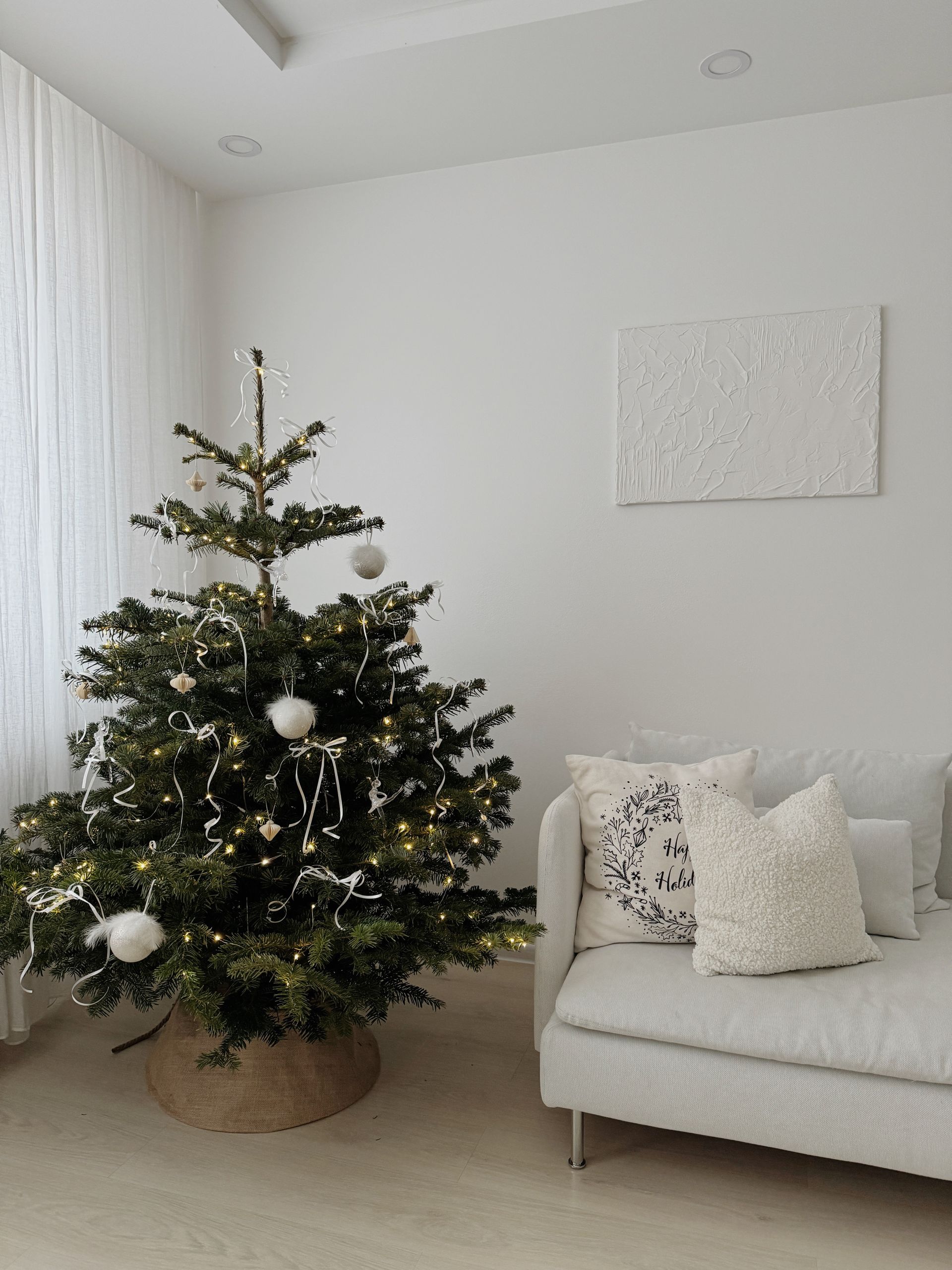 Minimalist Christmas tree with white decorations in a bright living room.