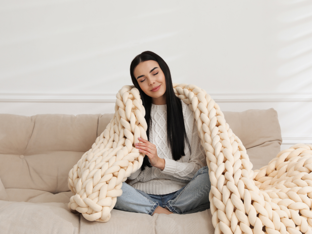 Oversized cable knit throw draped over a woman grey/ beige sofa