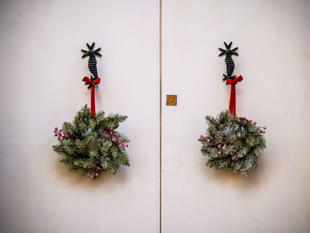 Twin Christmas wreaths with red ribbons elegantly hang on a white door, evoking holiday cheer.