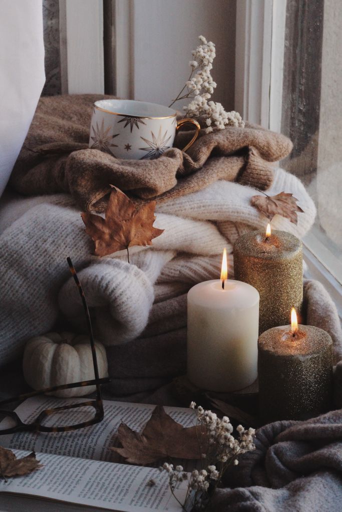 Warm autumn scene with candles, sweaters, and dry leaves by the window, creating a cozy ambiance.
