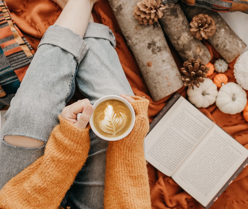 Warm cosy autumn scene with latte art coffee, book, and cozy sweater in an inviting atmosphere.