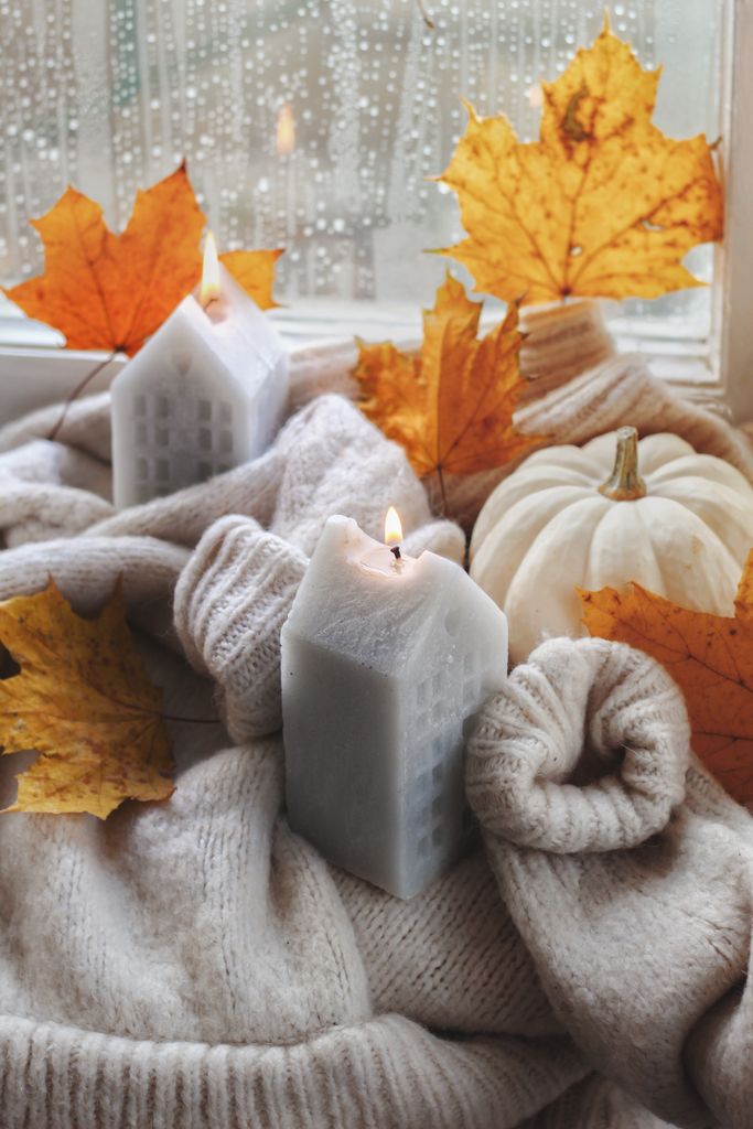 Warm cozy autumn scene with candles, leaves, and pumpkin on windowsill.