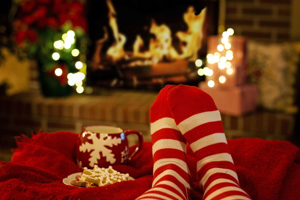 Warm holiday scene with striped socks, a mug, and cookies by a fireplace watching Christmas Movies