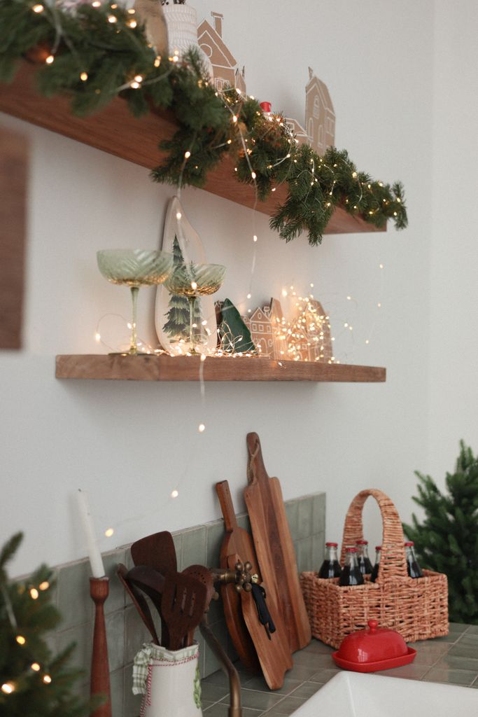 Warm kitchen shelves decorated with holiday lights and greenery, evoking a festive atmosphere.