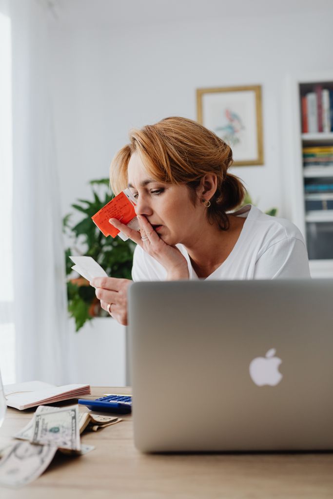 Woman concerned over finances with laptop, card, and receipts. Indoor, modern home office setting.
