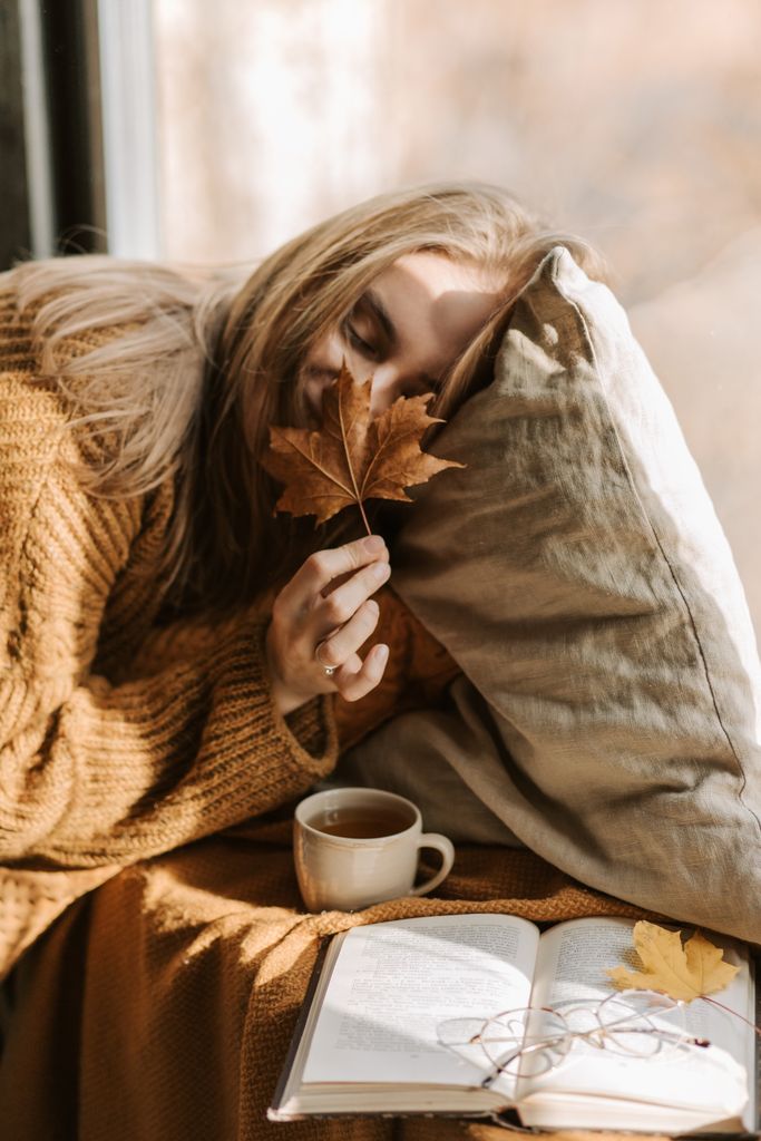 Woman enjoying a peaceful fall day indoors with a warm drink and book.
