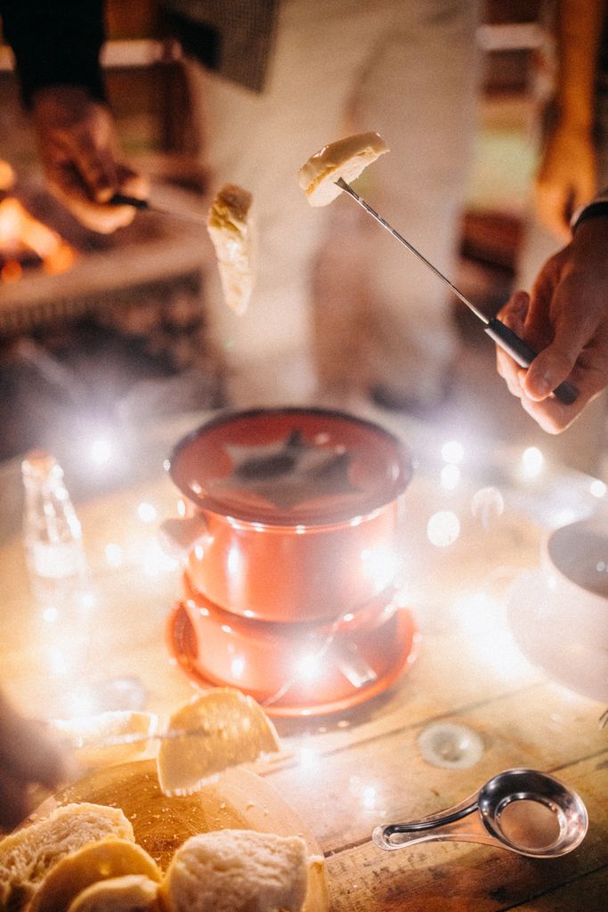 A couple sharing melting cheese in fondue and eating bread on a romantic autumn date night at home