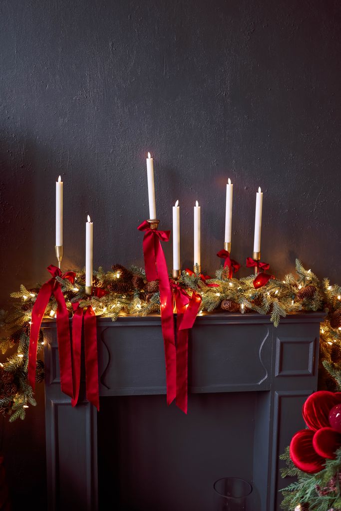 Festive Christmas mantel decorated with candles, red ribbons, and greenery for a cozy holiday atmosphere.