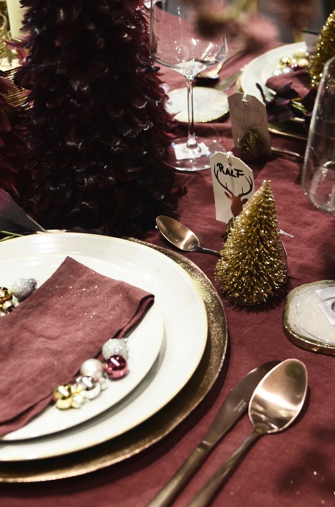 From above of dishware with textile napkin between baubles near cutlery and decorative Christmas trees on table