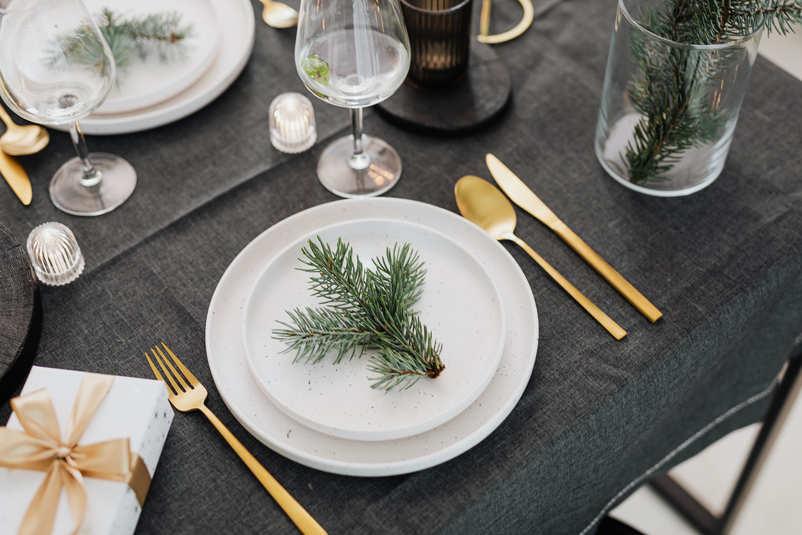 Stylish holiday table setup with evergreen branches and gold cutlery.