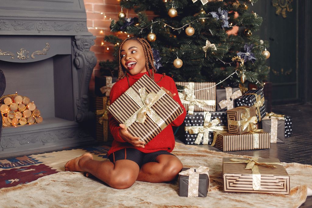 Young woman celebrating Christmas with gifts by the tree in a cozy living room.