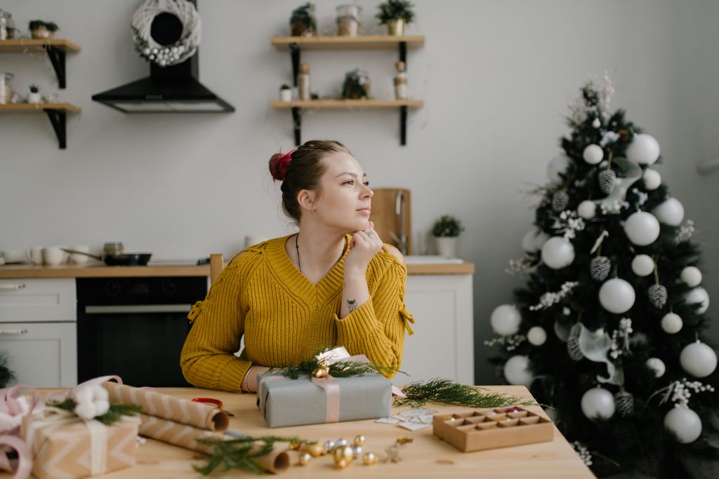 Young woman in cozy sweater daydreams about what to buy her daughter for Christmas.