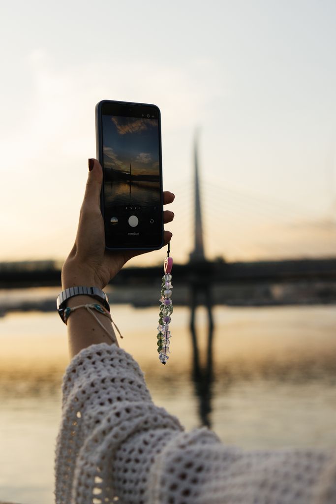 A person holds an iphone with a beaded charm 