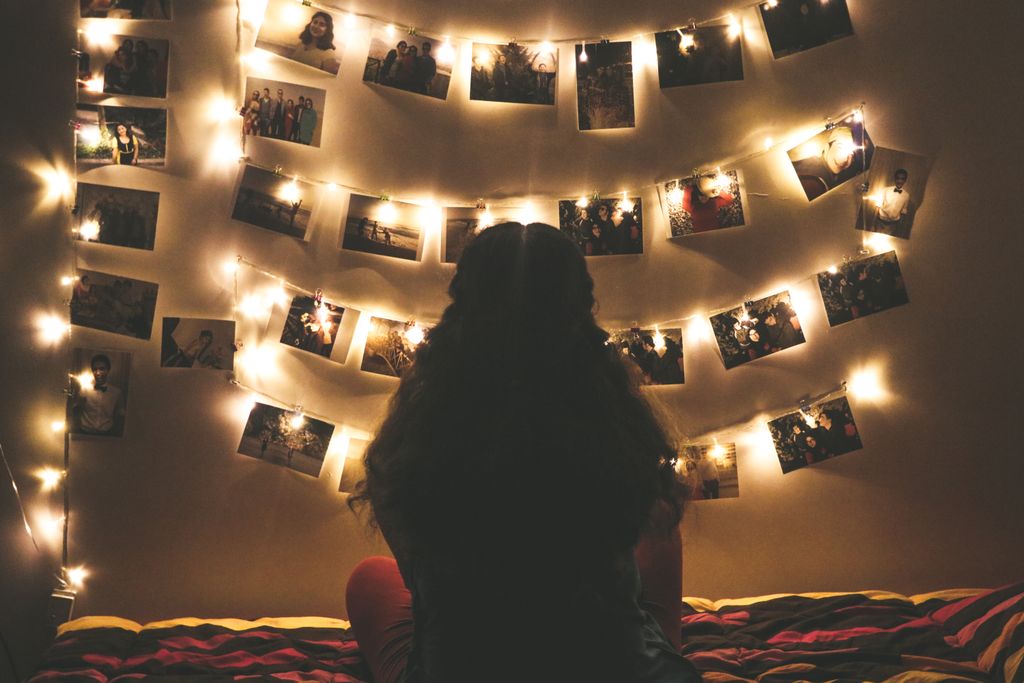 A warmly lit bedroom featuring string lights and a woman viewing hanging photos.