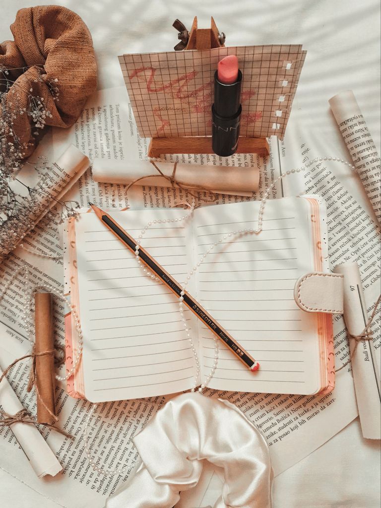Aesthetic flat lay with a notebook, lipstick, and decorative elements like pearls and scrunchies.