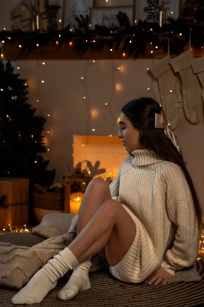 Woman in knit sweater enjoys a cozy winter evening with festive Christmas lights.